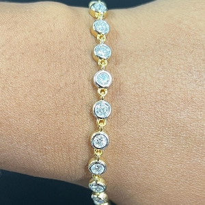 May include: A gold chain bracelet featuring a series of round, bezel-set clear stones. Each stone is encased in a polished gold setting, connected by small gold links, creating a continuous line of circular accents along the length of the bracelet.