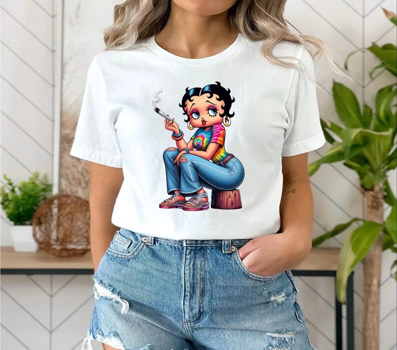 May include: White t-shirt featuring a cartoon illustration of a woman with black hair, wearing a tie-dye shirt, blue jeans, and red sandals. The character is holding a lit cigarette. The design is printed on a white t-shirt.