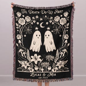 May include: A black and cream woven throw blanket featuring two ghosts in the center, surrounded by roses, spiderwebs, stars, a crescent moon, and mushrooms. The text reads "TIL DEATH DO US PART" at the top and "LUCAS & MIA est 2022" at the bottom.
