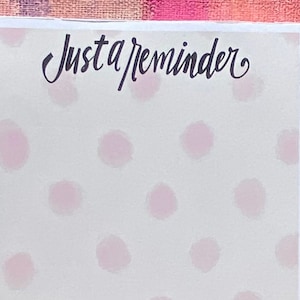 May include: A white card with pink polka dots and the text "Just a reminder" in black cursive. The bottom of the card has a border of pink roses with green leaves.