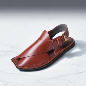 May include: A brown leather sandal with a square toe and a strap that goes around the ankle. The sandal has a buckle closure and a black sole. The leather is a rich, reddish-brown color.