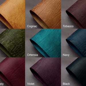 May include: Nine swatches of textured leather in various colors. Colors include Olmo, Cognac, Tobacco, Olive, Ortensia, Navy, Burgundy, Violet, and Black. Each swatch is folded to show the material's texture and color variations.