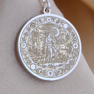 Op de afbeelding: Een zilveren hangerketting met een gedetailleerde cirkelvormige bedel. De bedel heeft een gegraveerd ontwerp van een figuur in een bosscène, omgeven door een decoratieve rand. De hanger hangt aan een fijne zilveren ketting.