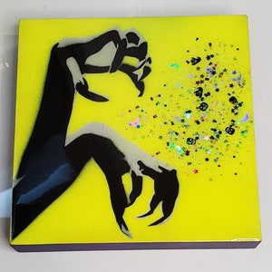 May include: A black silhouette of a hand reaching out towards a yellow background with scattered glitter. The glitter is in the shape of stars, moons, and other abstract shapes.