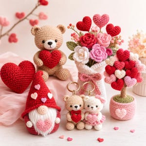 Peut inclure: Une collection d'objets au crochet comprenant un ours en peluche beige tenant un cœur rouge, un gnome au chapeau rouge, un bouquet de fleurs et cœurs en crochet dans un vase blanc, un arbre en forme de cœur et deux petits porte-clés ours.