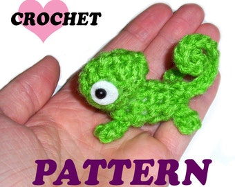 May include: A green crocheted chameleon with white eyes. The chameleon is sitting in the palm of a hand. The text "CROCHET PATTERN" is written below the chameleon.