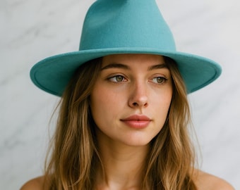 Pode incluir: Um chapéu fedora turquesa com aba larga. O chapéu é feito de feltro e tem uma coroa clássica em forma de lágrima. O chapéu é de cor sólida e é usado por uma pessoa com cabelo longo e castanho claro.