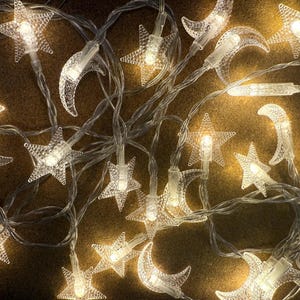Könnte beinhalten: Lichterkette mit Sternen und Monden aus klarem Kunststoff. Die Lichter strahlen warmweiß. Die Lichterkette mit transparentem Draht eignet sich für dekorative Zwecke. Ideal für eine festliche Atmosphäre.