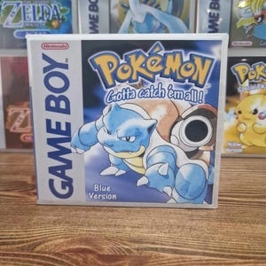May include: A Game Boy video game cartridge for Pokémon Blue Version. The box features a blue Blastoise character with the text "Pokémon Gotta catch 'em all!" and "Blue Version". Other Pokémon game boxes are visible in the background.