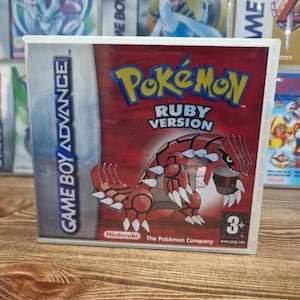 May include: A Game Boy Advance video game cartridge for Pokémon Ruby Version. The game case is red with the Pokémon logo and a graphic of a red and white creature. The case is in a clear plastic case.