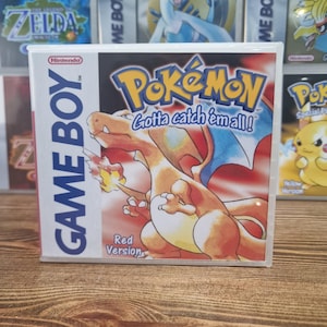 May include: A Game Boy Pokémon Red Version video game cartridge. The box features a red and orange Charizard with blue wings. The Pokémon logo is in yellow and blue, with the tagline "Gotta catch 'em all!"