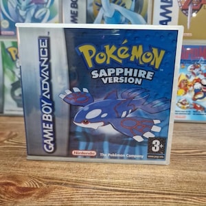 Op de afbeelding: Game Boy Advance game case voor Pokémon Sapphire Version. De case heeft een blauwe en witte Kyogre illustratie en het Pokémon logo in geel. De game is geschikt voor kinderen vanaf 3 jaar.