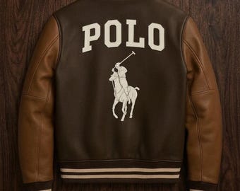 Op de afbeelding: Bruin en bruinleren jas met het woord "POLO" in witte blokletters op de rug. Een witte afbeelding van een polospeler op een paard staat eronder. De jas heeft bruine mouwen en gestreepte randen.