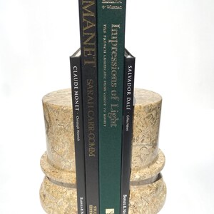 Puede incluir: Dos sujetalibros cil&iacute;ndricos de piedra beige con patr&oacute;n de f&oacute;siles que sostienen cuatro libros de tapa dura. Los libros se titulan Manet, Sarah Carr-Gomm, Impressions of Light y Salvador Dal&iacute;. Los sujetalibros tienen un dise&ntilde;o de base circular escalonada.