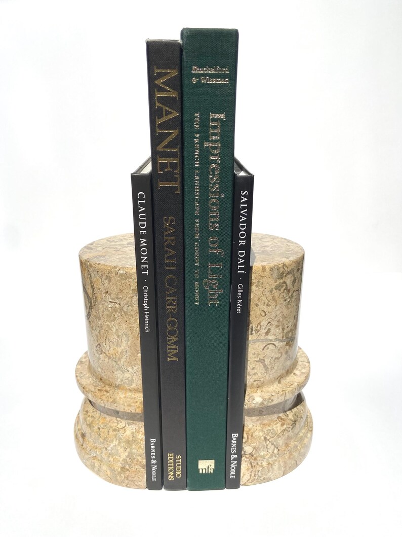 Puede incluir: Dos sujetalibros cil&iacute;ndricos de piedra beige con patr&oacute;n de f&oacute;siles que sostienen cuatro libros de tapa dura. Los libros se titulan Manet, Sarah Carr-Gomm, Impressions of Light y Salvador Dal&iacute;. Los sujetalibros tienen un dise&ntilde;o de base circular escalonada.