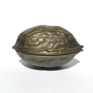 May include: A bronze-colored, walnut-shaped trinket box. The box is made of metal and has a textured surface, with a hinged lid. The box is designed to resemble a walnut shell, with detailed ridges and a naturalistic appearance.