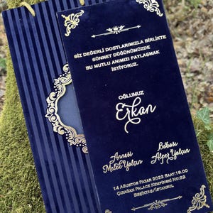 May include: Navy blue invitation with gold detailing. The invitation has gold text and decorative flourishes. The invitation is for a circumcision celebration and includes the names of the parents and son, along with the date, time, and location.