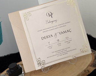 May include: A square cream-colored wedding invitation card with gold foil accents and ornate corner details. The text reads Evleniyoruz, Derya & Yamaç, and includes event details for a ceremony at The Marmara Esma Sultan on April 17, 2029.