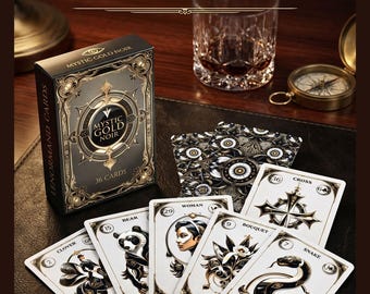 May include: A deck of Mystic Gold Noir Lenormand cards with 36 cards, featuring gold and black designs. The cards are spread out, showcasing illustrations of a bear, woman, snake, and other symbols. The box is visible, along with a glass and compass.