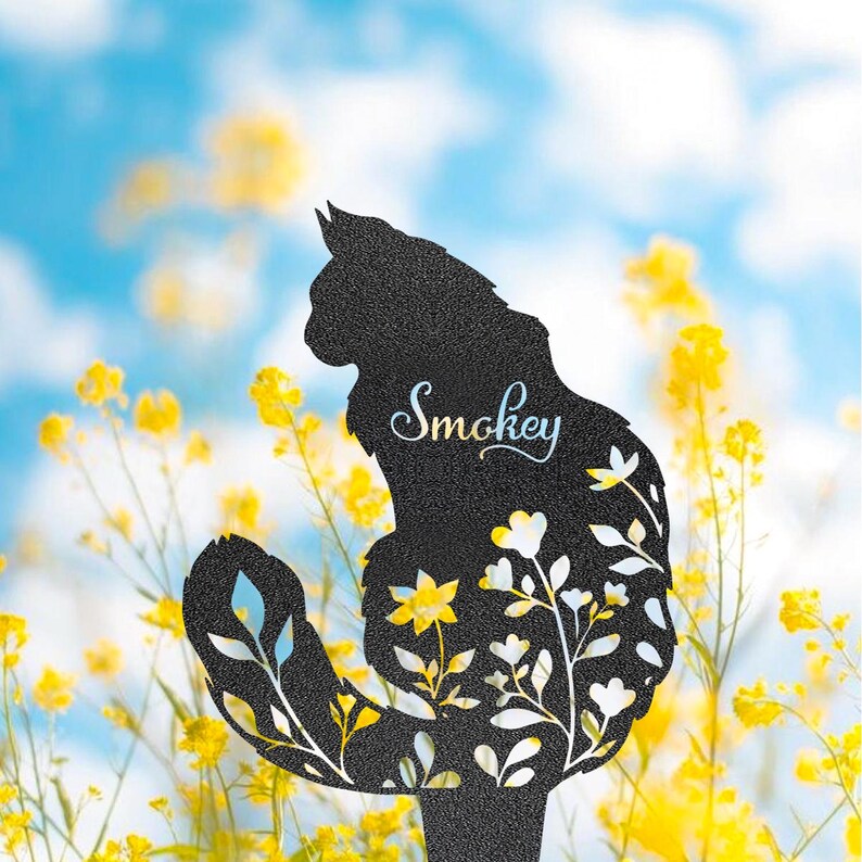 May include: Black metal cat silhouette garden stake with floral cutouts. The cat's name, "Smokey," is scripted on the body. The background features yellow flowers and a blue sky.