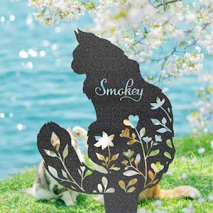 May include: Black metal cat silhouette garden stake with the name "Smokey" in cursive script. The cat's body features floral cutouts with gold and white accents. A cat is visible in the background.