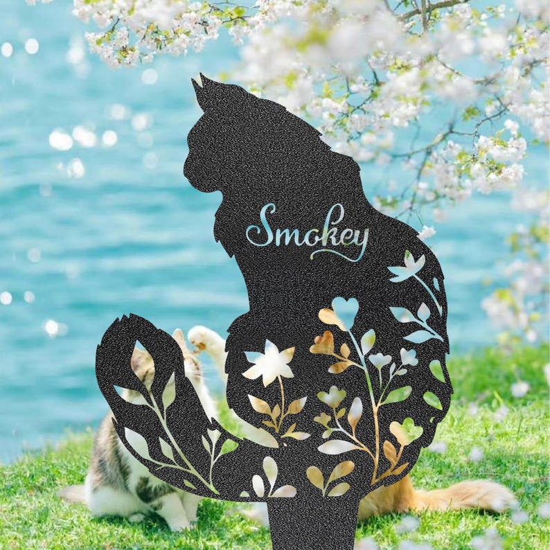 May include: Black metal cat silhouette garden stake with the name "Smokey" in cursive script. The cat's body features floral cutouts with gold and white accents. A cat is visible in the background.