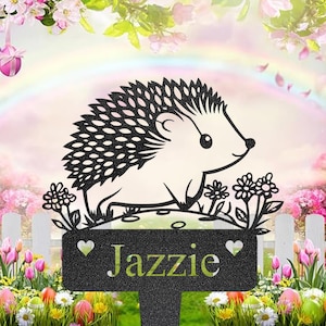 Puede incluir: Estaca de jardín de metal negro con un diseño de erizo recortado y el nombre "Jazzie" en verde. La estaca incluye detalles florales y de corazón, ideal para la decoración exterior.