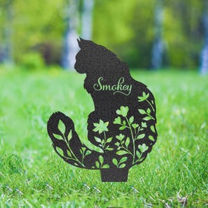 May include: Black metal cat silhouette garden stake with floral cutouts. The cat's name, "Smokey," is written in cursive. The stake is designed to be placed in a garden or lawn, adding a decorative touch to outdoor spaces.