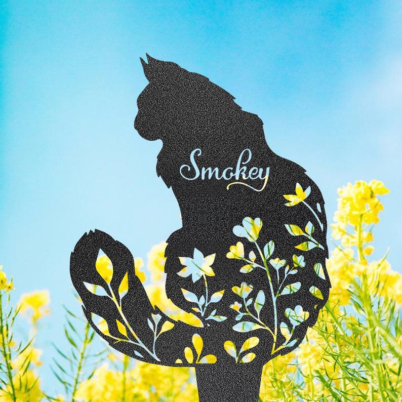 May include: Black metal cat silhouette garden stake with the name "Smokey" in cursive script. The cat is decorated with cut-out floral designs with yellow and white accents. The background features yellow flowers and a blue sky.
