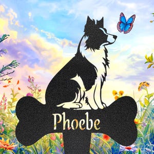 May include: A black and white metal dog silhouette garden stake with the name "Phoebe" on a bone-shaped sign. A blue butterfly hovers near the dog, set against a colourful sky and floral background.