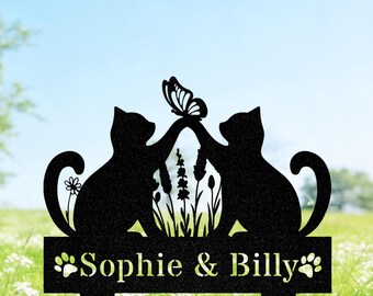 May include: Black metal garden stake featuring two cat silhouettes reaching for a butterfly. The design includes the names "Sophie & Billy" and paw prints. The background shows a field of white flowers and a blue sky.
