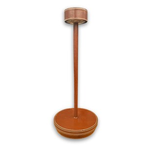 Peut inclure: Un porte-chapeau en cuir marron avec une base ronde et un dessus cylindrique. Le support est en bois et en cuir, avec des détails de couture blancs. Le support mesure environ 152 cm de haut.