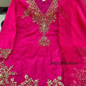 May include: A bright fuchsia outfit with elaborate gold embroidery. The V-neck top and matching scarf display detailed floral designs. The text "Jaipuriboutique" is visible on the garment.