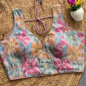 Könnte beinhalten: Ärmelloses Oberteil mit floralem Muster in Pastellfarben, darunter Rosa, Blau und Orange. Das Oberteil hat einen V-Ausschnitt und einen Bindverschluss am Rücken. Der Stoff ist mit Pailletten verziert. Der Text "Jaipuriboutique" ist sichtbar.