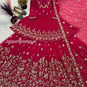 May include: A vibrant fuchsia-colored ensemble featuring intricate gold embroidery. The outfit includes a long-sleeved top with a V-neck and a tiered skirt. The text "Jaipuri Boutique" is visible. A matching dupatta completes the look.