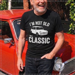 May include: A black short-sleeve t-shirt featuring a white graphic of a vintage compact car in the center. Above the car, the text reads I'M NOT OLD, and below the car, the text reads I'M A CLASSIC. The design is printed in a distressed white font.