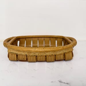 May include: A rectangular, woven basket with rounded handles. The basket is made of light brown rattan and has a textured surface. The open design allows for easy viewing of contents. Ideal for storage or display.
