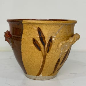 Könnte beinhalten: Ein handgefertigter Keramiktopf mit zweifarbigem Design. Der Topf hat ein braunes und beiges Farbschema mit blattartigen Mustern. Er hat zwei Griffe und eine weite Öffnung, geeignet für Pflanzen oder zur Aufbewahrung.