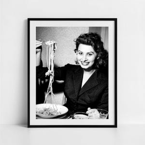 Könnte beinhalten: Schwarz-Weiß-Druck in einem Rahmen einer lächelnden Frau, die eine Gabel voll Spaghetti hochhält. Sie trägt einen Nadelstreifenblazer und sitzt an einem Tisch mit einer Schüssel Pasta und einem Glas.
