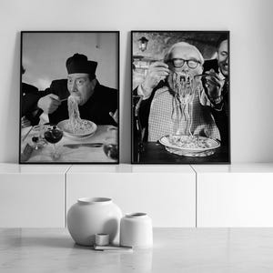 May include: Two framed monochrome photographs of people eating spaghetti. The first shows a person in a dark outfit and hat. The second shows a person wearing glasses and a patterned shirt. A white vase and two smaller containers are in the foreground.