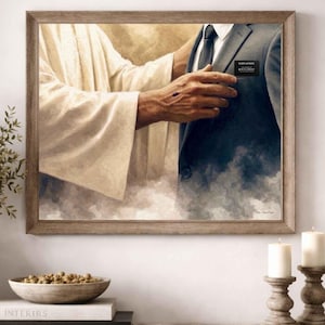 Peut inclure: Œuvre d'art encadrée représentant une scène religieuse. Une figure en robes blanches touche l'épaule d'une personne en costume sombre. Le costume porte une étiquette nominative qui indique "Elder Johnson". L'œuvre est dans un cadre en bois.