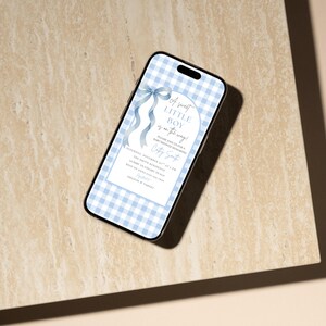 May include: A smartphone screen shows a baby shower invitation with a blue and white gingham pattern. The invitation text reads "A sweet LITTLE BOY is on the way!" with event details. A blue ribbon and text are featured.