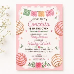 May include: A rectangular baby shower invitation card with a pink border, featuring illustrations of four concha sweet breads, colorful papel picado bunting, and floral accents. The text reads: A SWEET LITTLE Conchita IS IN THE OVEN! PLEASE JOIN US FOR A Baby Shower HONORING Hailey Cruise SATURDAY, AUGUST 8TH AT 5:00 PM 123 CONCHITA WAY, SWEET, TX 76134 RSVP JEN (123)456-7890 REGISTERED AT AMAZON & TARGET.