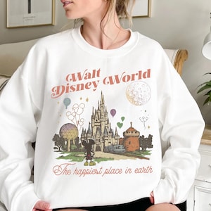 May include: White sweatshirt featuring a vintage-style graphic of Cinderella's castle, Mickey Mouse, and the text "Walt Disney World" and "The happiest place in earth". The design includes colorful balloons and a stylized moon.