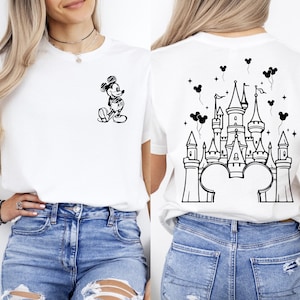 Puede incluir: Camiseta blanca con una ilustraci&oacute;n en blanco y negro de Mickey Mouse en la parte delantera. La parte trasera de la camiseta muestra un dise&ntilde;o de castillo en blanco y negro con orejas de Mickey Mouse, estrellas y globos.