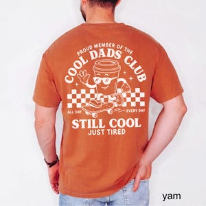 Pu&ograve; includere: T-shirt arancione bruciato con una grafica di una tazza di caff&egrave; su uno skateboard e la scritta "COOL DADS CLUB". La maglietta include anche le frasi "ALL DAY EVERY DAY" e "STILL COOL JUST TIRED".