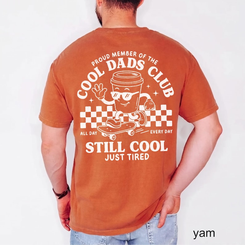 Pu&ograve; includere: T-shirt arancione bruciato con una grafica di una tazza di caff&egrave; su uno skateboard e la scritta "COOL DADS CLUB". La maglietta include anche le frasi "ALL DAY EVERY DAY" e "STILL COOL JUST TIRED".