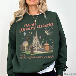 May include: Forest green sweatshirt with a vintage-style Walt Disney World graphic. The design includes the castle, Mickey Mouse, balloons, and the phrase "The happiest place on earth" in a retro font.