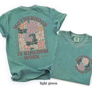 May include: Light green t-shirts featuring the text "MOTHERHOOD IS KINGDOM WORK" and a floral design. One shirt has the design on the back, the other on the front pocket. The design includes pink, orange, and brown flowers.