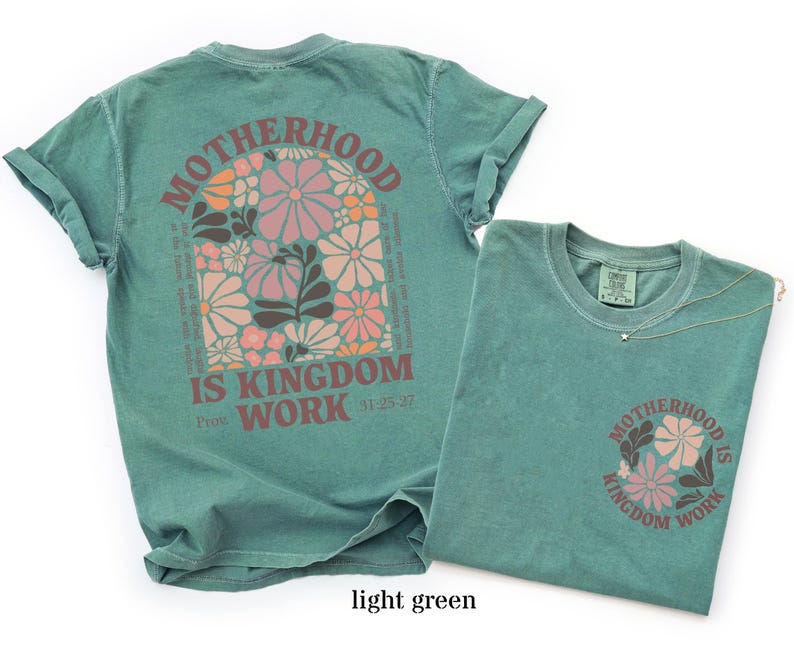 May include: Light green t-shirts featuring the text "MOTHERHOOD IS KINGDOM WORK" and a floral design. One shirt has the design on the back, the other on the front pocket. The design includes pink, orange, and brown flowers.